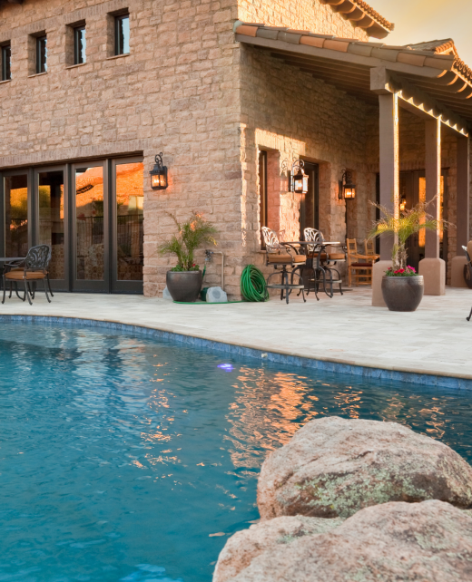 A two story texas brown brick home with a pool, during a sunset.